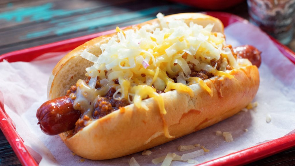 Close-up of a Cookout chili dog with toppings and melted cheese.